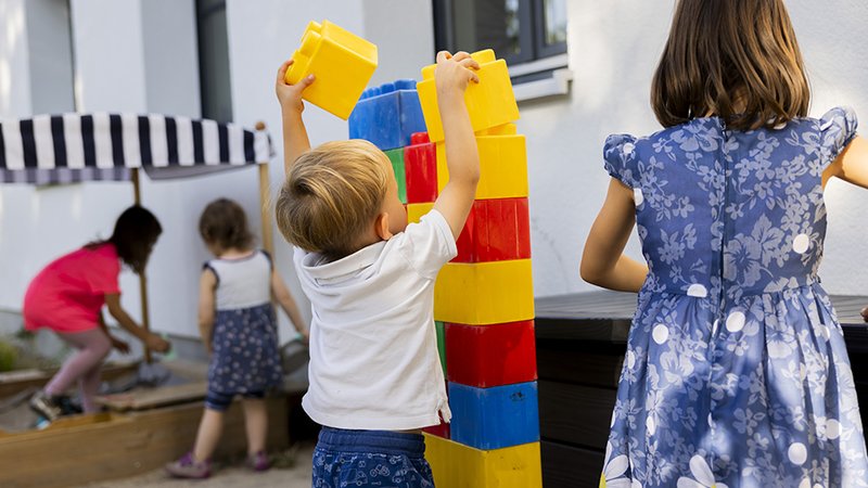 Kinder draußen mit Bausteinen/Sandkasten spielend: Spielmöglichkeiten im Garten des Nachbarschafts- / Familiencafés