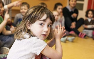 Kind sitzt im Kreis einer Gruppe und klatscht mit den Händen